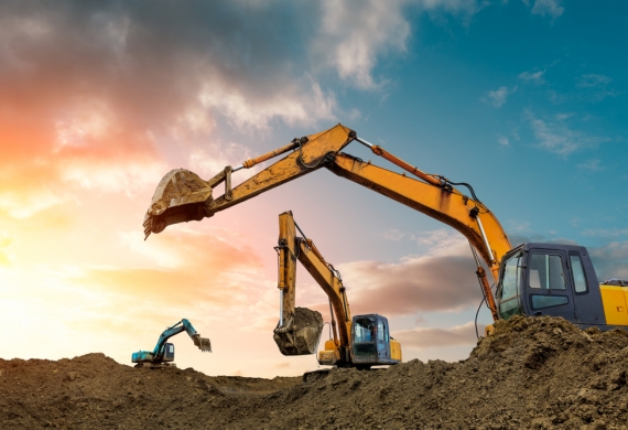 Three diggers digging up soil with sun shining in the background